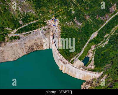 Vista aerea della diga di Stausee Mooserboden con acqua turchese, montagne verdi circostanti e attrezzature edili a Kaprun, Salisburgo, Austria. Foto Stock