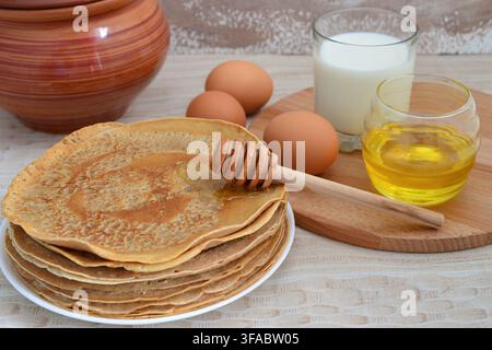 Pancake fatti in casa con miele, uova e un bicchiere di latte per la colazione Foto Stock