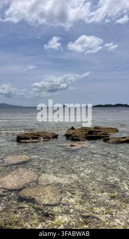 Acqua tropicale chiara e poco profonda scorre su una costa corallina rocciosa sotto un vasto cielo blu a Sulawesi, Indonesia. Foto Stock
