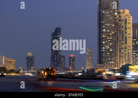 BANGKOK, THAILANDIA — 20 GENNAIO 2026: Le barche in movimento creano scie di luce sul fiume Chao Phraya sotto lo skyline illuminato dei grattacieli di Bangkok. Foto Stock