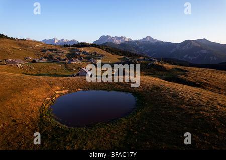 Tradizionali capanne di legno di pastori che si ergono sui pascoli alpini verdi del paesaggio scenografico dell'altopiano montuoso di Velika Planina, in Slovenia. Foto Stock