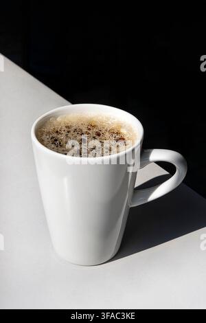 Tazza da caffè in ceramica bianca riempita con caffè nero appena preparato, illuminata dalla luce naturale del sole, concetto minimalista di bevanda Foto Stock