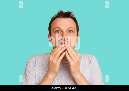 Gli occhi di un uomo sono spalancati per l'incredulità mentre si copre la bocca con entrambe le mani in un gesto di shock Foto Stock