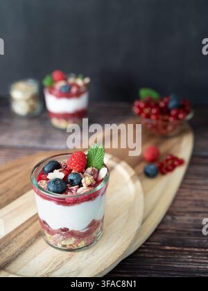 Dessert a strati con bacche di yogurt e granola croccante, stilizzato con oggetti rustici Foto Stock