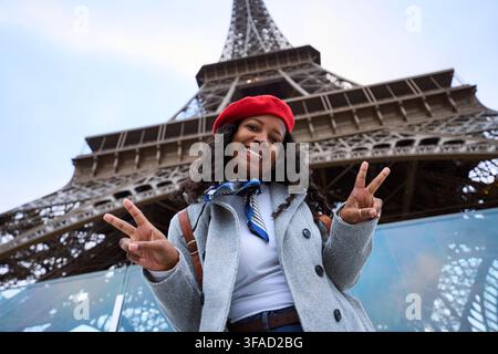 Giovane donna che gode di un viaggio a Parigi facendo il segno della pace alla telecamera Foto Stock