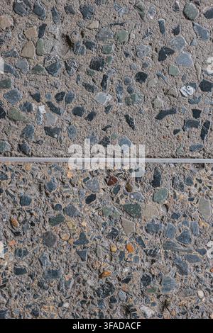 Schegge di pietra naturale multicolori in pavimentazione terrazzo grigia, divise da una linea di giunto Foto Stock