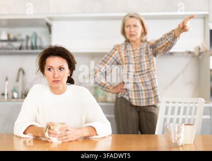 Sconvolta una donna di mezza età seduta al tavolo della cucina con la schiena alla vecchia che litiga con lei Foto Stock