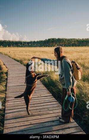 Donna che utilizza il rinforzo positivo per addestrare un cane a stare sulle zampe posteriori durante una passeggiata all'aperto su una passerella di legno Foto Stock
