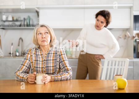Sconvolta la vecchia seduta al tavolo della cucina con le spalle a donna che litigano con lei Foto Stock