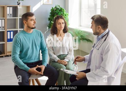 Sorridente felice giovane coppia seduta con un medico di famiglia maschile terapista in clinica medica. Foto Stock