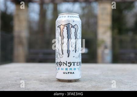 Lattina Monster Energy Ultra in primo piano. Bevanda energetica bianca Monster zero zucchero. Bevanda rinfrescante per uno stile di vita in piedi all'aperto in un ambiente di parco. Foto Stock