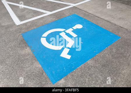 Spazio di parcheggio accessibile blu con un simbolo bianco di accessibilità per sedia a rotelle dipinto sul marciapiede in cemento. Foto Stock