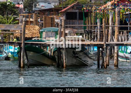 Molo di legno rustico su un lungomare tranquillo con decorazioni colorate appese, piccole barche e edifici sulla collina sullo sfondo in una giornata soleggiata Foto Stock