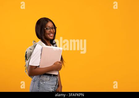 Allegra donna afroamericana con taccuino giallo, vista laterale Foto Stock