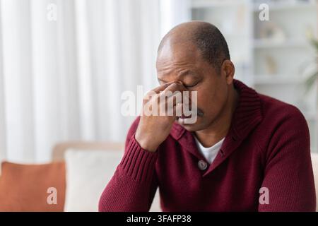Uomo nero maturo che si pizzica il ponte del naso, mostrando mal di testa Foto Stock