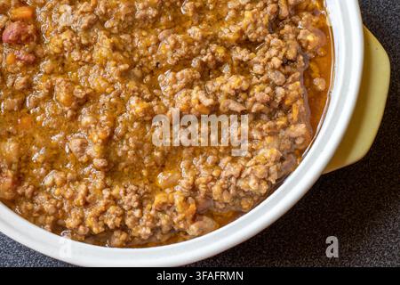 Prima vista di ragù di carne italiano cotto lentamente con carne tritata e verdure a cubetti in una pentola di ceramica bianca con manico giallo, angolazione alta Foto Stock