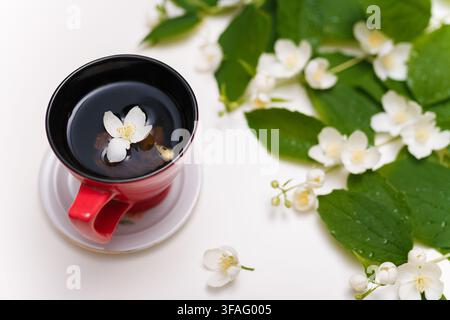 Tazza di tè al gelsomino. Alcuni fiori su sfondo bianco da tavolo. Bevande salutari, concetto di fioritura primaverile. Foto Stock