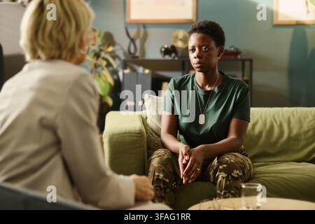 Giovane soldata afroamericana seduta su un divano durante una seduta di terapia con uno psicologo caucasico, discutendo di salute mentale e PTSD per i servizi di supporto militare Foto Stock
