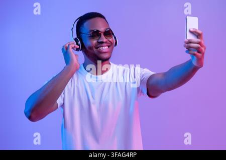 Bell'uomo nero che indossa cuffie wireless e occhiali da sole che prendono Selfie Sullo smartphone Foto Stock