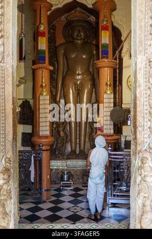 India. Stato del Madhya Pradesh. Khajuraho. Un fedele in abiti rituali bianchi prega davanti alla statua monumentale di un Tirthankara nel tempio di Shantinat Foto Stock