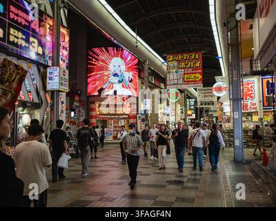 Acquistiatori che camminano attraverso il passaggio commerciale coperto Sennichimae con insegne al neon e schermi LED a Osaka, Giappone Foto Stock