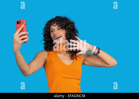 Giovane donna che fa una videochiamata e agita la mano con un'espressione felice Foto Stock