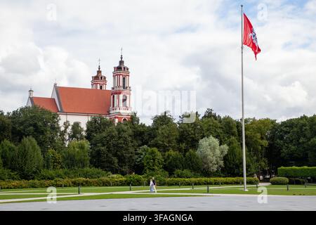 Chiesa di San Filippo e San Giacomo dietro Piazza Lukiškės a Vilnius, Lituania, accanto alla bandiera storica Vytis che sventola su un alto asta Foto Stock