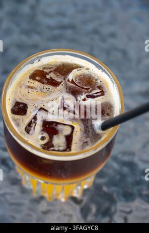 Vista dall'alto di una bevanda rinfrescante caffè freddo con cubetti di ghiaccio galleggianti, ricca crema di espresso e una cannuccia nera in un bicchiere sfaccettato su un testo Foto Stock