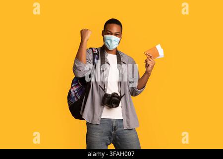 Felice entusiasta guy del turista africano in maschera medica con passaporto In mano Foto Stock
