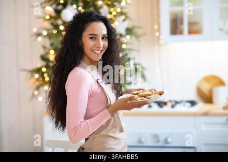 Gioiosa giovane donna in posa con piatto di biscotti a Cristmas Cucina decorata Foto Stock