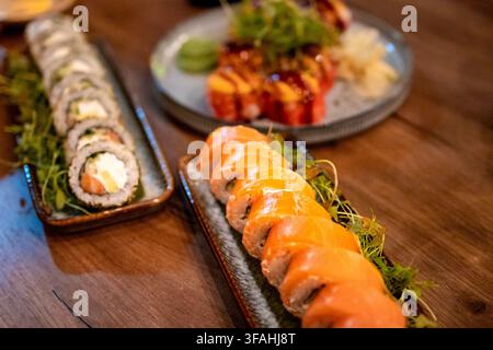 Vista ampia di un vassoio di sushi con rotoli classici e rotoli Philadelphia cotti al forno. Concetto di sushi giapponese per la ristorazione e la cultura alimentare asiatica. Foto Stock