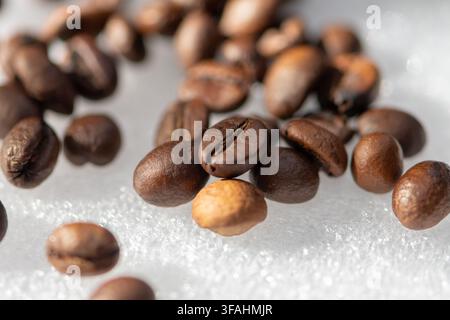 Grani di caffè tostati sparsi su una superficie riflettente luminosa in un primo piano macro. Foto Stock