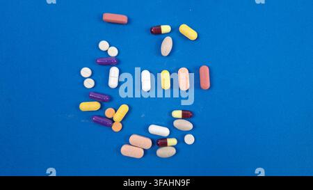 pillole, compresse e capsule sciolte in bianco, giallo, rosa e viola sparse su uno sfondo blu solido per concetti farmaceutici e sanitari. Foto Stock