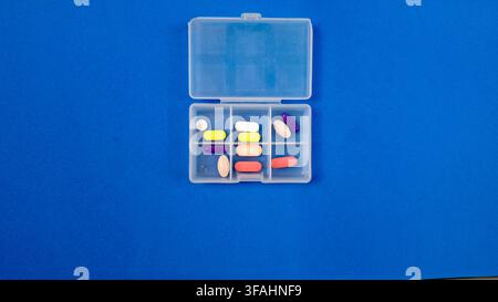 Organizer per pillole con compresse bianche e capsule su sfondo blu Foto Stock