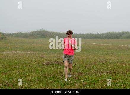 Donna che si gode l'allenamento mattutino, corre all'aperto in un campo verde con nebbia Foto Stock