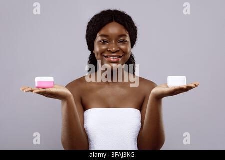 Attraente Black Lady avvolto in Towel che tiene due vasi con Creme idratanti Foto Stock