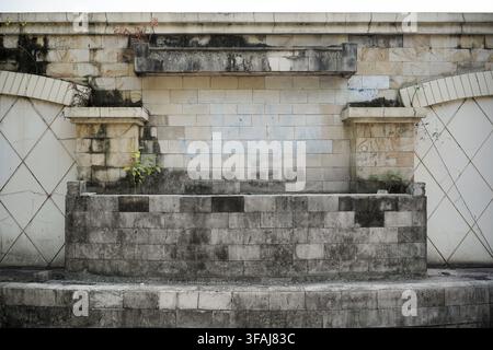 Vista frontale di una vecchia struttura esterna abbandonata con un muro di blocchi di pietra consumato, una vasca per piante vuota, macchie d'acqua, sporcizia. Foto Stock