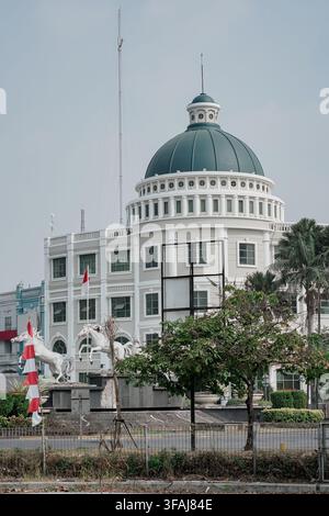Vista esterna di un maestoso monumento in statua di cavallo bianco e di una bandiera nazionale indonesiana rossa e bianca sventolante posizionata davanti a un grande edificio classico Foto Stock