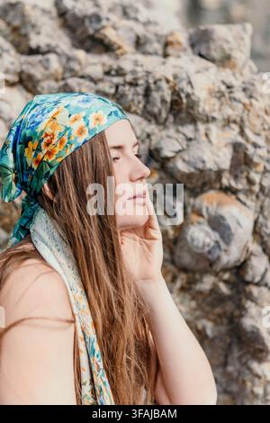 Ritratto di donna, giovane donna con foulard floreale in posa su uno sfondo roccioso, con gli occhi chiusi e un'espressione serena Foto Stock