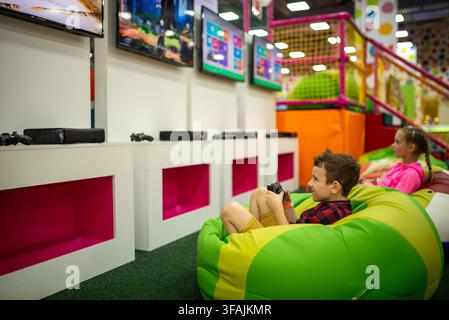 Bambini che tengono i controller e giocano ai videogiochi sui pouf Foto Stock