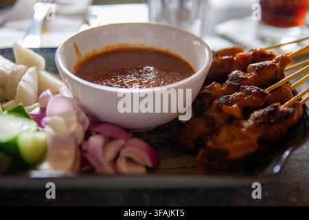 Un piatto tradizionale di spiedini di pollo satay grigliati serviti con una ricca salsa di arachidi, cetrioli affettati, cipolle e focaccine di riso (nasi impit) a Foto Stock
