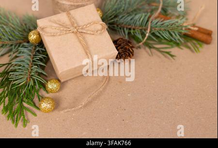 Regalo di carta kraft legato con spago accanto a ramo di pino, pigna e ornamenti dorati su sfondo marrone texturizzato Foto Stock