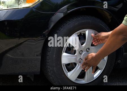 Prima piano delle mani di una persona che installa o rimuove un cerchione argentato su un pneumatico nero di un'auto durante la manutenzione del veicolo. Foto Stock