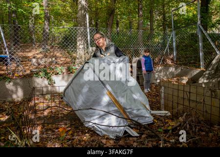 Una donna e un bambino si trovano tra le tombe di un cimitero boscoso durante l'autunno. Foto Stock