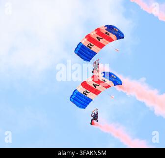 Squadra di paracadutismo dei Royal Air Force Falcons che scende in formazione con paracaduti rossi, bianchi e blu e scie di fumo rosa durante una dimostrazione aerea Foto Stock