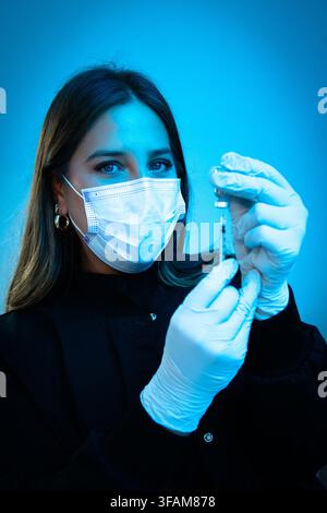 Medico mascherato che tiene una siringa e una fiala di medicinale Foto Stock