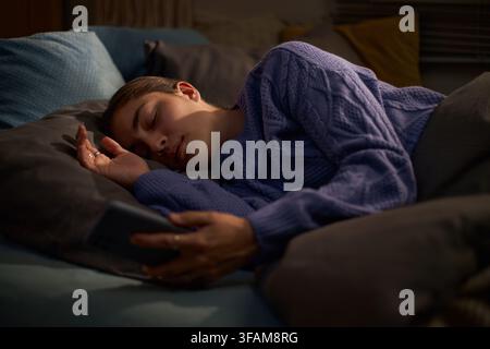 Donna che dorme a letto mentre tiene uno smartphone in mano Foto Stock