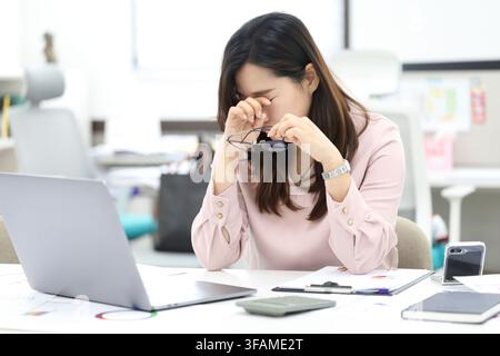 Dipendente d'ufficio coreano che soffre di affaticamento oculare e usa gli occhiali mentre legge documenti Foto Stock