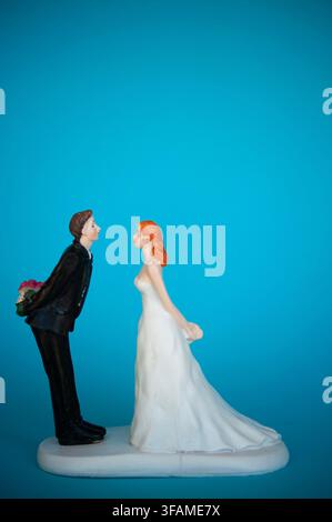 Decorazione per torta nuziale di una sposa e uno sposo che si affrontano, con lo sposo che nasconde fiori dietro la schiena su uno sfondo blu brillante Foto Stock