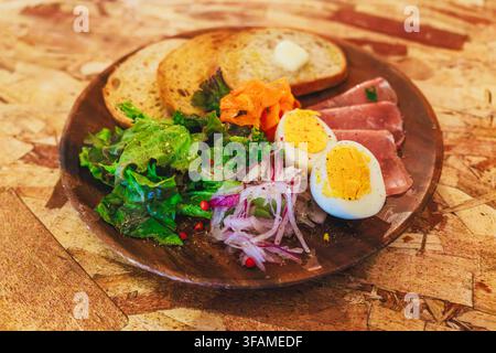 Piatto di colazione gourmet fresco con uova sode affettate, prosciutto, pane al lievito madre tostato, carote sottaceto, cipolle e insalata verde croccante Foto Stock